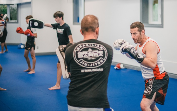 An adult throwing a strike on focus mitts during Muay Thai pad work at Gracie Barra Manotick